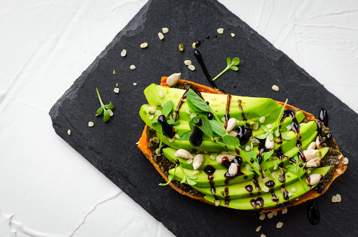 Healthy avocado toasts on sweet potato for breakfast or lunch with vegan pesto, microgreens, sliced avocado, hemp and sunflower seeds. Vegetarian food. Clean eating. Top view. Copy space.