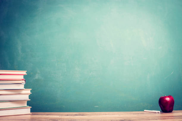 istock Textbooks, red apple on wooden school desk with chalkboard. 1154081807