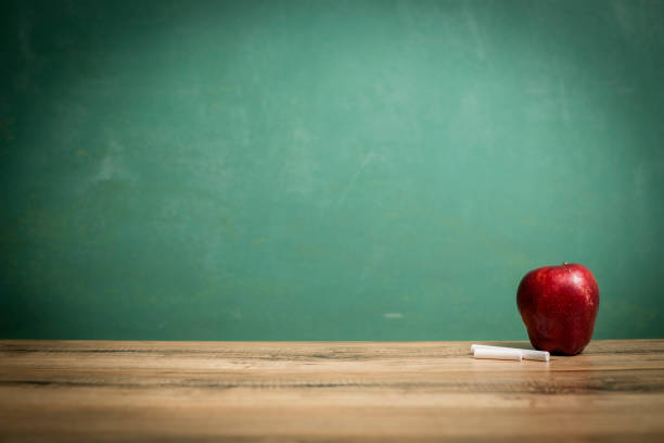 istock Apple, chalk on wooden school desk with chalkboard. 1154082033