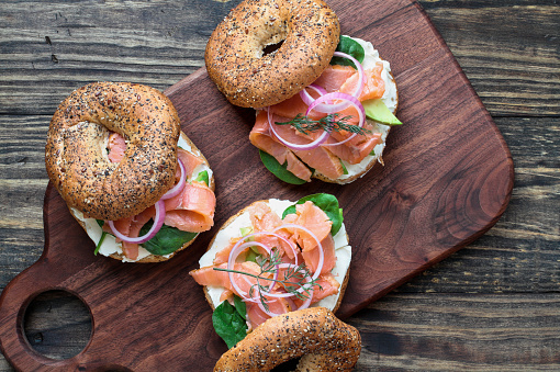 Lox - Everything bagel with smoked salmon, spinach, red onions, avocado and cream cheese over a rustic wood table background. Image shot from top view or flat lay position.
