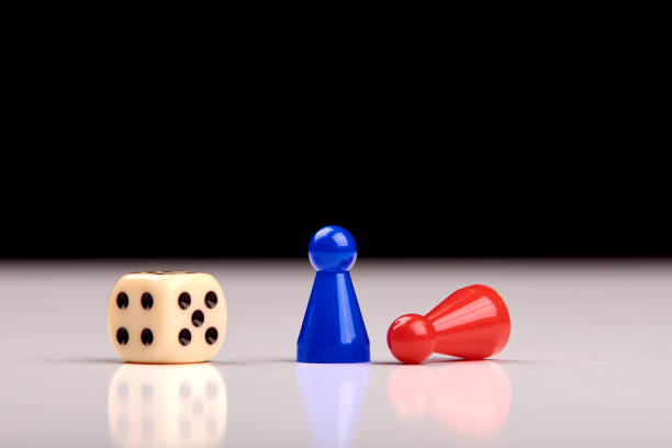 istock Standing blue playing figurine as winner and lying red figurine as loser with playing dice on white table top with black background. Space for your text. 1154087407