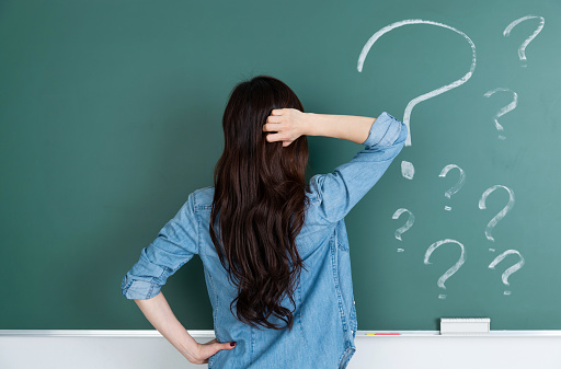 Woman in front of blackboard with question marks.