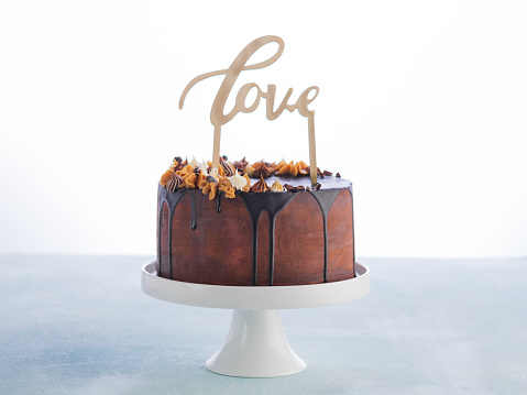 Drip Cake with melting chocolate ganache and love wood caketopper on a white background with space for text. Valentines day Celebration concept. Trendy Drip Cake.