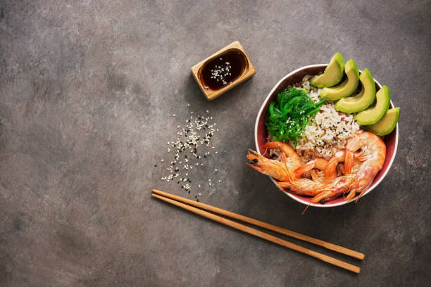 Shrimp poke bowl, rice, avocado, chuka, soy sauce and sesame on a dark rustic background. Top view, flat lay, copy space. Shrimp poke bowl, rice, avocado, chuka, soy sauce and sesame on a dark rustic background. Top view, flat lay, copy space avocado brown stock pictures, royalty-free photos & images