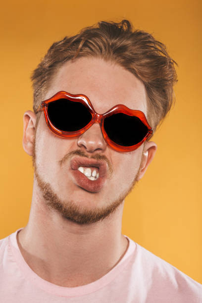 istock Grimacing young man in lip shaped sunglasses on yellow background 1154096303