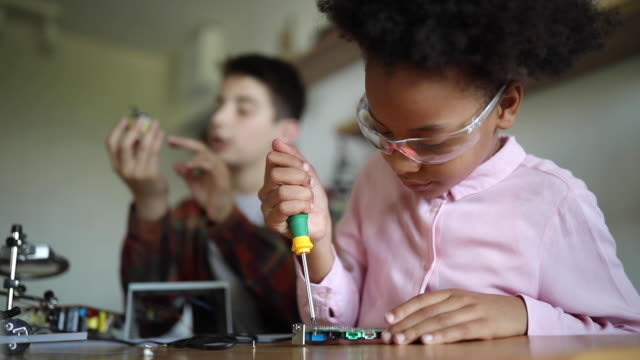 Schoolboy and mixed race schoolgirl working together on school science project, using screwdrivers, wearing protective eyeglasses, low angle view