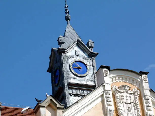 retro style simple blue tower clock with yellow hands in zink color metal facade. fine stucco finish in foreground on freshly renovated old small town city hall under clear blue sky