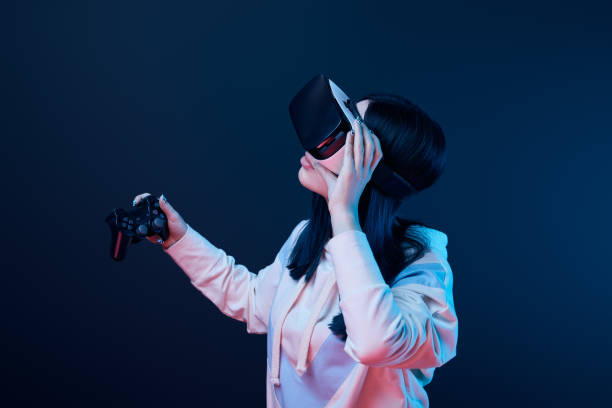 istock KYIV, UKRAINE - APRIL 5, 2019: Brunette woman holding joystick while touching virtual reality headset on blue 1154112268