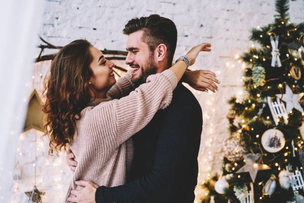 istock Happy romantic couple hugging standing near decorated christmas tree enjoying spending time together, charming woman looking at her boyfriend with love celebrating New Year day together at home 1154116540