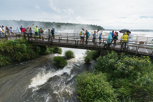 Puerto Iguazu, Argentina - March 16, 2019: Group of tourists looking at the waterfalls of Iguazu on the border of Argentina and Brazil on a bright spring day.