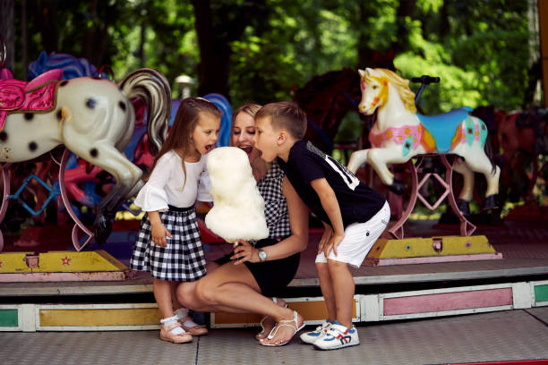 Happy family eating cotton candy at an amusement park. Mother, son and daughter biting candyfloss. Happy family eating cotton candy at an amusement park. Mother, son and daughter biting candyfloss. child cotton candy stock pictures, royalty-free photos & images