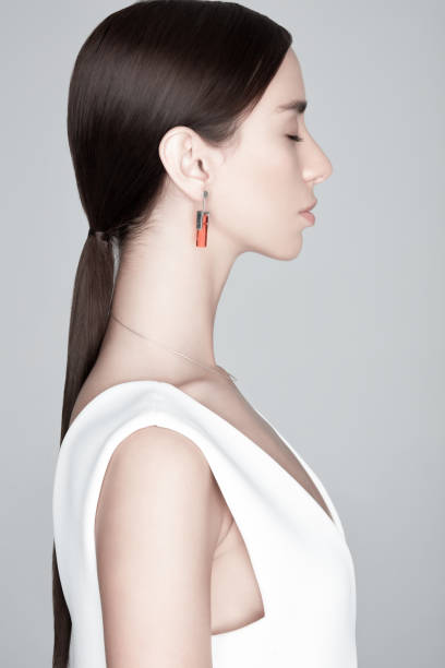 Side view of young charming woman with earring with orange gemstone in stylish dress with closed eyes on gray background