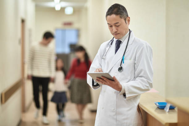 Japanese Male Doctor Checking Medical Data on Digital Tablet