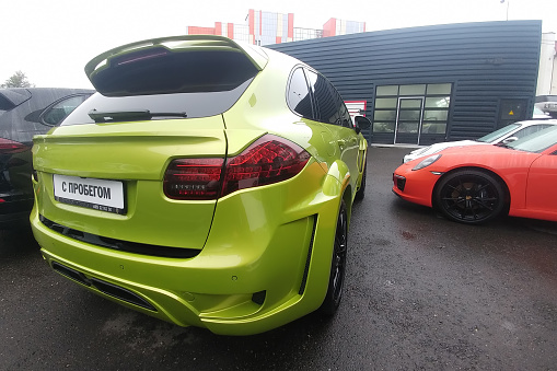 Moscow, Russia - May 05, 2019: Lime Green Tuned Porsche Cayenne with wide kit by Hamman, modified hood, pad on the fifth door. Nearby is a red Porsche 911 Back side view