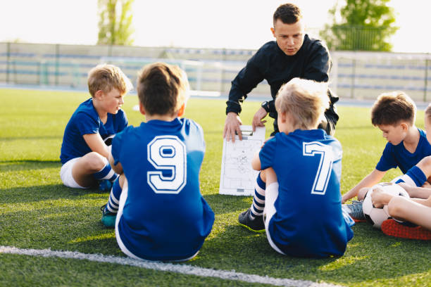 football coach coaching kids. soccer football training session for young boys. young coach teaching children on football field. football tactic education. coach explains the strategy of the game - youth league imagens e fotografias de stock