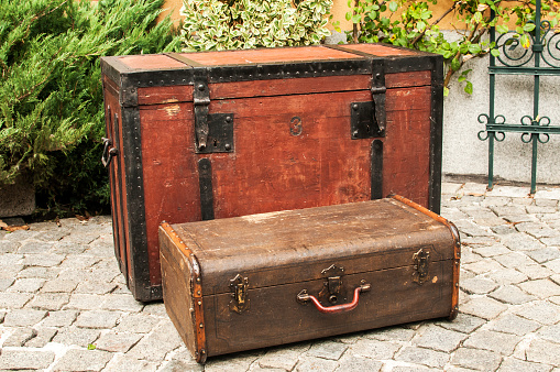 Old retro wooden chest and vintage grunge suitcase isolated on stone paved house backyard