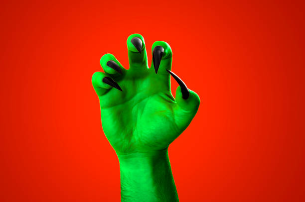 Halloween, nightmare creature and evil monster horror story concept with a scary zombie or demon hand with creepy long black nails isolated on orange background with a clipping path cut out halloween, criatura de pesadilla y el concepto de historia de terror de monstruos malvados con un zombi aterrador o una mano demoníaca con uñas negras largas y espeluznantes aisladas sobre fondo anaranjado con un recorte de trayectoria de clip