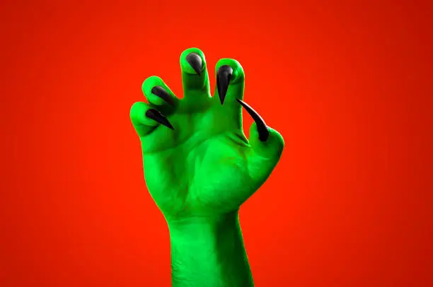 Halloween, nightmare creature and evil monster horror story concept with a scary zombie or demon hand with creepy long black nails isolated on orange background with a clipping path cut out