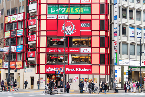 Tokyo, Japan - March 30, 2019: Shinjuku street sidewalk with many people near entrance to Wendy's fast food restaurant with sign for first kitchen