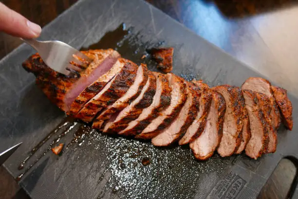 Grilled pork tenderloin, sliced, on a black cutting board