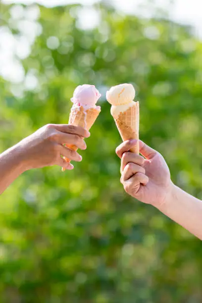 Photo of woman holding and eating ice cream in the park. Hands holding melting ice cream waffle cone in hand on summer nature light  background.