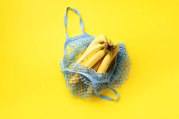istock Organic banana in mesh string bag on yellow paper background. Flat lay, top view. Zero waste, plastic free concept. Healthy clean eating diet and detox. Summer food 1154314052