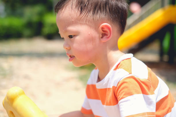 Cute little Asian 2 - 3 years old toddler boy child sweating during having fun playing, exercising outdoor at playground, Heat stroke concept Cute little Asian 2 - 3 years old toddler baby boy child sweating during having fun playing, exercising outdoor at playground on nature at park, Heat stroke and summer sunstroke risk symptom concept hyperthermia photos stock pictures, royalty-free photos & images