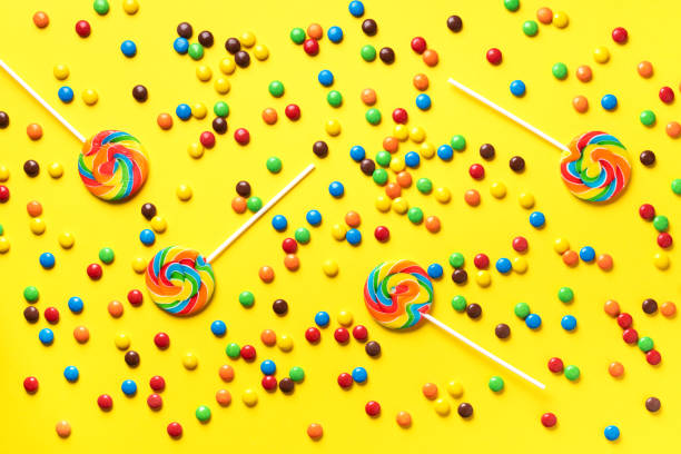 lollipop colorido, doces coloridos do arco-íris no fundo amarelo. textura doce revestida das partes do chocolate. vista de cima. flat lay. confetti para feriados, conceito da festa de anos - summer photography organic outdoors - fotografias e filmes do acervo