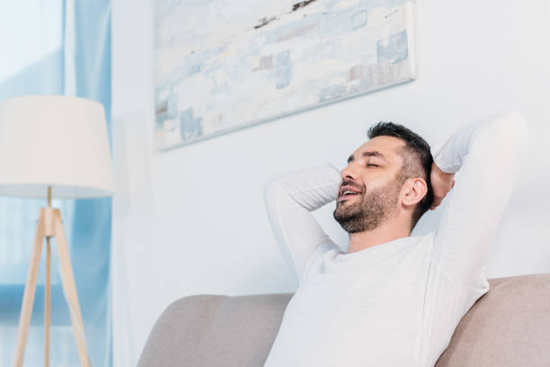 istock handsome bearded man with eyes closed and Hands Behind Back resting on couch at home with copy space 1154319627
