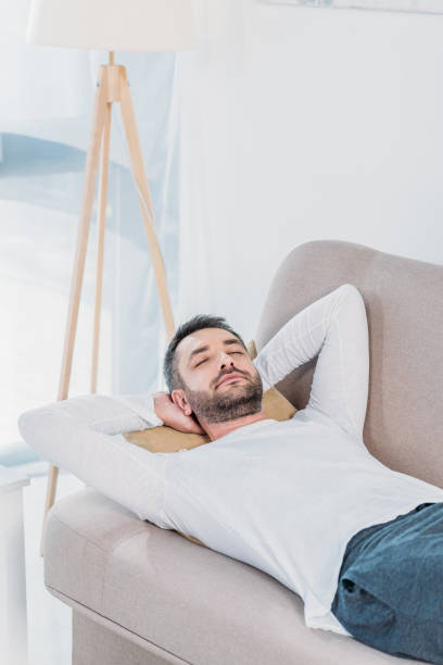 istock handsome bearded man with eyes closed and Hands Behind Back sleeping on couch at home 1154319650