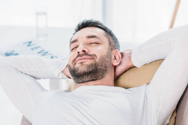 istock selective focus of handsome bearded man with eyes closed and Hands Behind Back resting on couch at home 1154319657