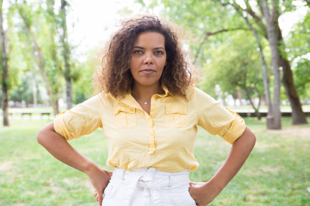 istock Serious woman keeping hands on hips and posing at camera in park 1154319910