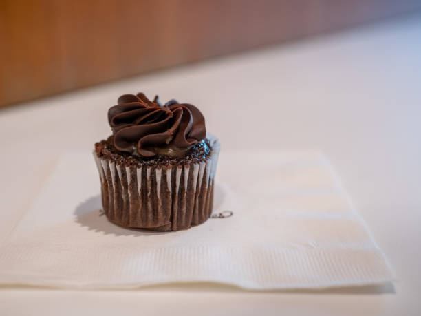 istock Small black chocolate cupcake sitting on napkin in on bakery table 1154323398