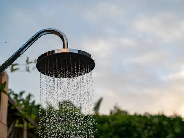 Waterfall showerhead outside in evening sky with water streaming down