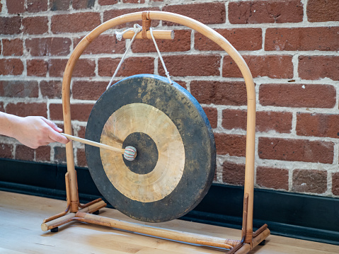 Small suspended gong sitting hit with mallet by hand of woman