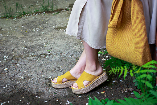 Summer fashion outfit. Girl in dress, yellow shoes and trendy knitted bag, a side view