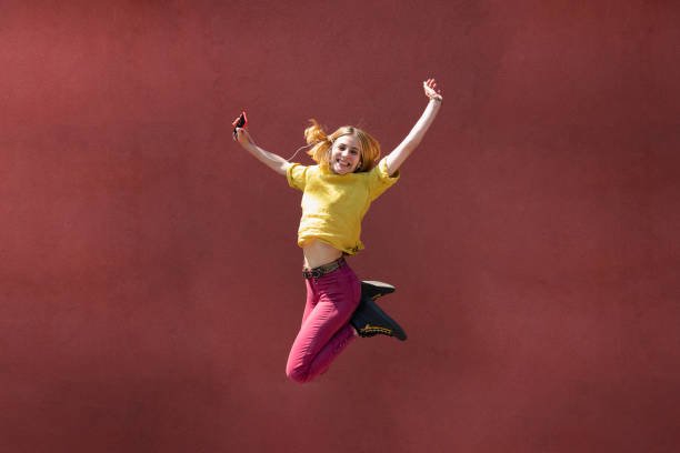 istock Happy Young Woman Jumping, Coral Colored Wall 1154327026