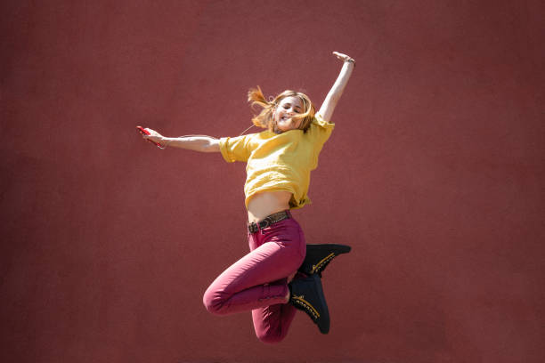 Happy young woman jumping, coral colored wall background