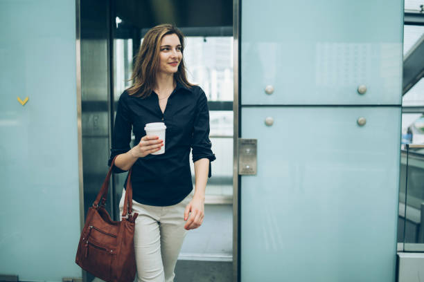 Woman leaving elevator, holding coffee cup Woman leaving elevator, holding coffee cup. outdoor elevator stock pictures, royalty-free photos & images