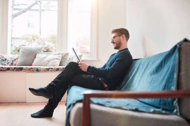 istock Young man relaxing at home, reading on a digital tablet. 1154328771