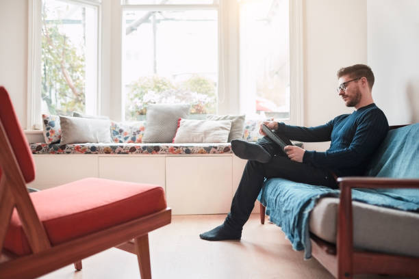istock Young man relaxing at home, reading on a digital tablet. 1154328799