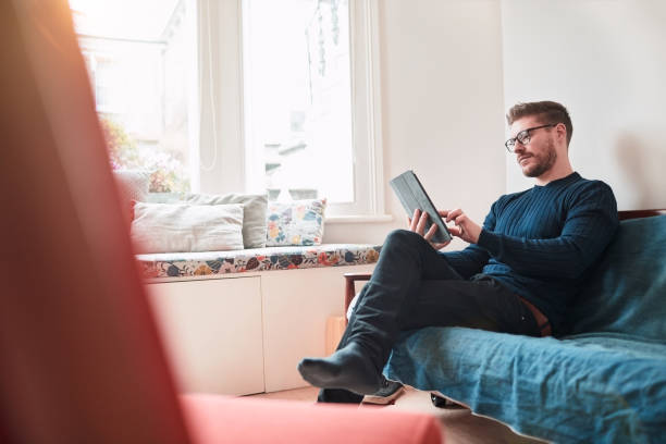 istock Young man relaxing at home, reading on a digital tablet. 1154328835