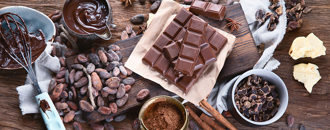 Cacao beans, powder, cacao butter,  chocolate bar and chocolate sauce on wooden background. Panorama, banner\
