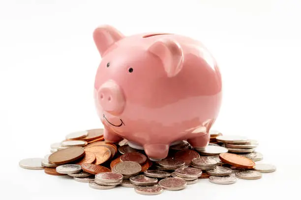 Photo of Save money, financial planning of personal finances and being thrifty concept theme with a pink piggy bank sitting on a pile of bronze and silver colored coins isolated on white background