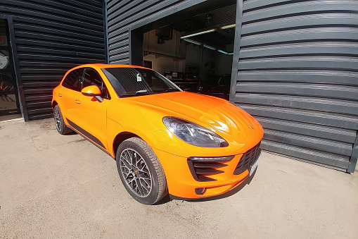 Moscow, Russia - April 29, 2019: Orange Porsche Macan S on the street. Parked car tuned by colored protective film. Front side view. Car is wrapped by special film and parket near garage.