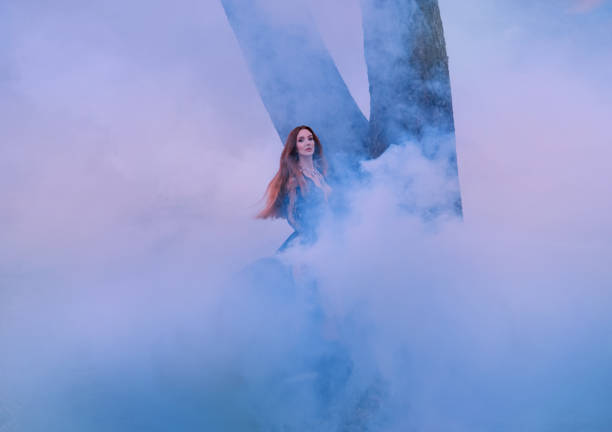 istock Witch in a black dress with a deep neckline conjures a whirlwind. Countess Dracula, a seductive vampire walking in thick fog, long red hair flying in the wind. The dark queen with a mysterious soul 1154356347