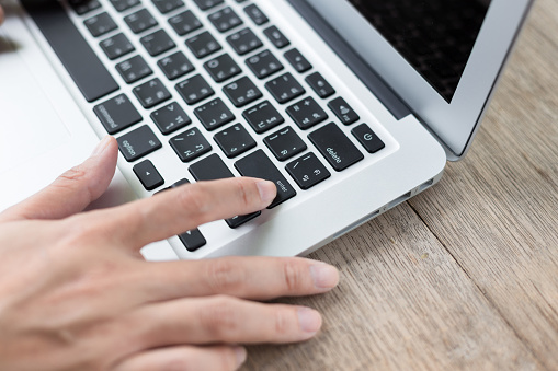 Woman hand pressing a Enter button on a laptop on the wood table background