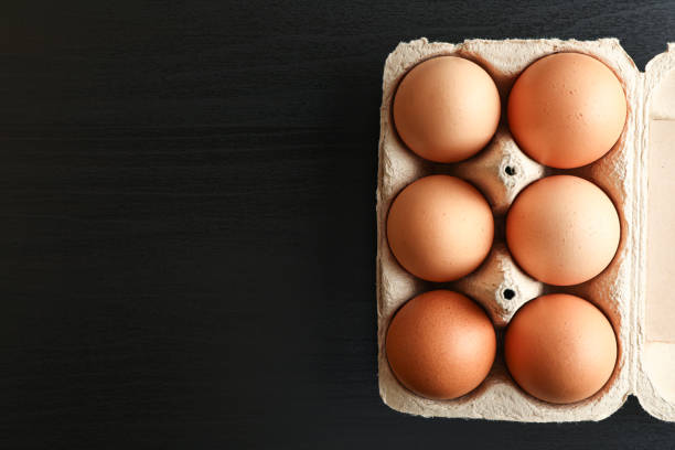 istock Brown chicken eggs in carton box on black background, space for text and top view 1154371753