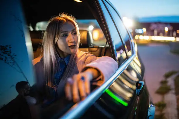 Beautiful woman driving on back seat of a car at night, looking through window