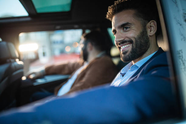 Gentleman in suit ride sharing with his friend Handsome bearded man in suit sitting on back seat in car with male friend, looking through window and smiling car city urban scene commuter stock pictures, royalty-free photos & images
